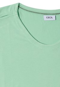 T-shirt en coton vert clair avec un col rond et une étiquette blanche cousue à l’intérieur affichant le nom de la marque "CECIL".
