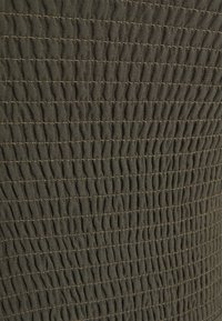 Tejido verde oliva con pliegues elásticos horizontales, muy juntos, que crean una textura fruncida y líneas de costura visibles.