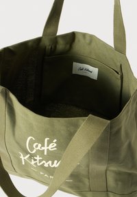 Zöld vászontáska, fehér nyomtatott logóval. Belsejében egy kis zseb található, és masszív szövetpántokkal rendelkezik.