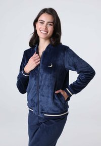 Giacca zip-up blu navy in tessuto morbido, con ricamo di una luna crescente sul lato sinistro del petto e dettagli a righe sui polsini e sull'orlo.