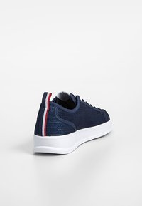 Basket bleu marine avec semelle blanche et lacets blancs, avec une languette rayée rouge, blanche et bleue au talon, vue de l'arrière côté gauche.