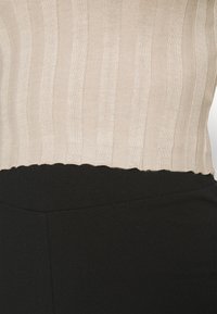 Haut beige à côtes avec une finition en dentelle, associé à un pantalon noir ajusté. Le tissu semble doux avec une texture.