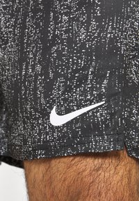Schwarze Shorts mit einem strukturierten, abstrakten weißen Muster. Verfügt über ein weißes Nike-Logo am Saum. Das Material scheint leicht und langlebig zu sein.