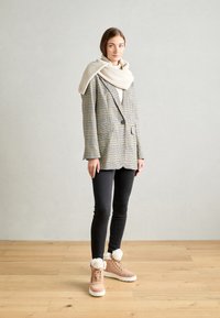 Blazer de cuadro en tonos beige y negro, acompañado de una bufanda crema, jeans skinny negros y botas rosas empolvadas con acentos de pelo sintético.