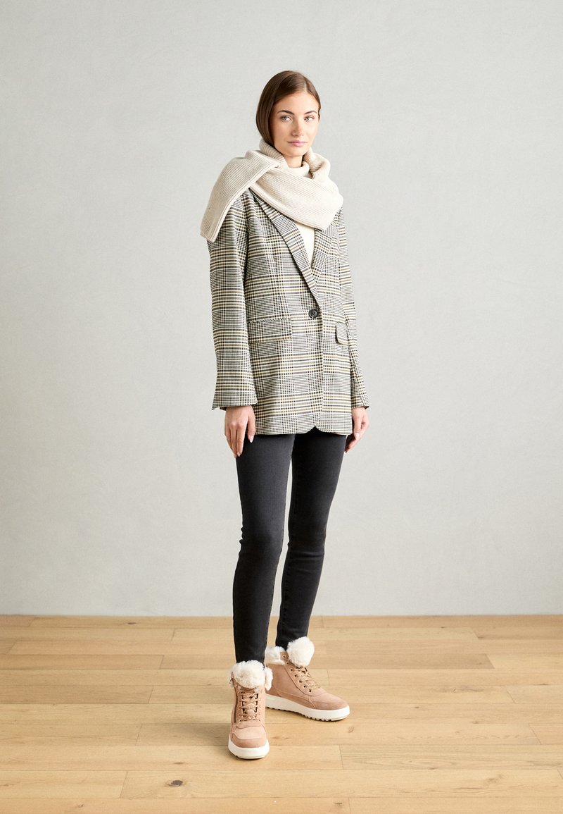 Blazer mit Karomuster in Beige- und Schwarztönen, kombiniert mit einem cremefarbenen Schal, schwarzen Skinny-Jeans und blassrosa Stiefeln mit Kunstfell-Akzenten.