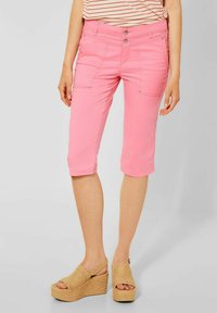 Pantaloni capri rosa chiaro con tasche frontali e chiusura a bottone, realizzati in tessuto morbido; abbinati a sandali con zeppa color beige e una maglietta a righe.