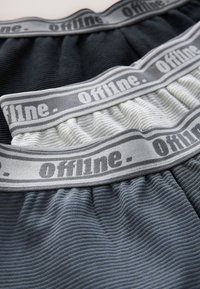 Trois boxers en tissu côtelé pliés en noir, blanc et gris avec des ceintures grises portant l'inscription "offline".