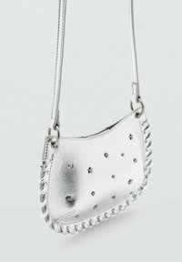 Strieborná kožená kabelka na rameno s hviezdovými výrezmi a kovovými detailmi. Má opletený okraj a tenký nastaviteľný remienok. Kompaktný dizajn.