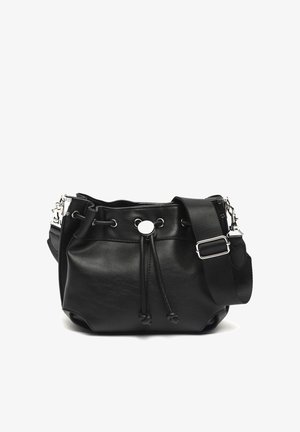 Sac seau en cuir noir avec bandoulière large en tissu réglable, ferrures argentées, et fermeture à cordon avec détail de bouton en métal.