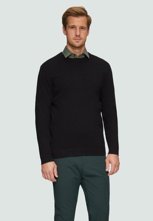 Zwarte gebreide sweater met een ronde hals, lange mouwen en geribbelde zoom. Draagt over een groen geruit overhemd, gecombineerd met donkergroene broeken.