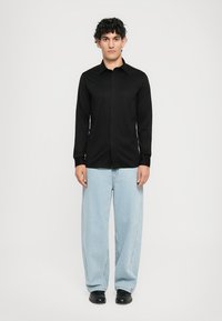Svart langermet skjorte med knappert krage, kombinert med lyseblå bred ben-jeans og svarte sko. Enkelt og strukturert design.