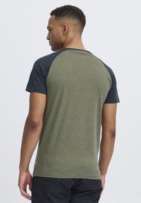 Short-sleeve t-shirt featuring a green body with dark blue raglan sleeves, made of soft fabric with a plain texture.