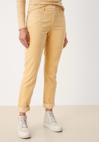 Pantaloni in corduroy gialli con risvolti, dotati di una progettazione a cinque tasche e chiusura con bottone, abbinati a sneakers bianche alte.