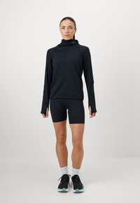 Camisola atlética preta de manga longa com gola alta, combinada com calções pretos. Apresenta um design justo e sapatilhas desportivas com detalhes em azul-água.