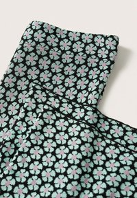 Gros plan d’un tissu à petit motif floral bleu canard et violet sur fond noir, montrant les détails de la ceinture et de la couture d’un vêtement.