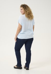 Top corto a maniche corte, di un blu chiaro e tessuto strutturato, con orlo arricciato; abbinato a jeans slim-fit di colore blu scuro e sandali con platform neri.