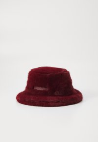 Burgunderfarget faux fur bøttehatt med myk tekstur, rund krone og bred floppy brem. Har et lærmerke på siden.