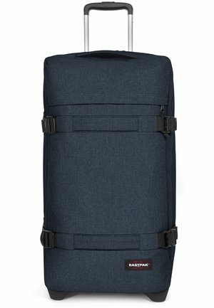 Maleta rodante de tela azul marino con correas ajustables, un asa extensible, una base robusta y un parche de logo en el lado.
