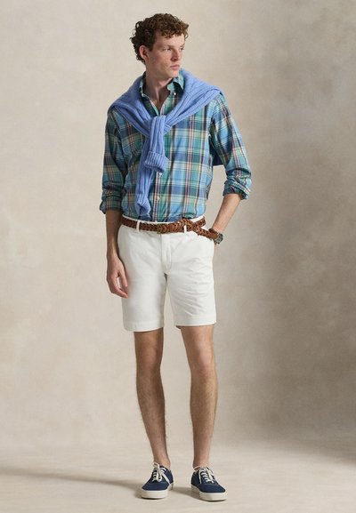 Plaid button-up shirt in blue and green, white shorts, brown braided belt, blue sweater tied around shoulders, navy canvas sneakers.