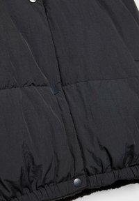 Czarna kurtka puchowa z pikowaną teksturą i zapięciem na zatrzaski. Materiał wydaje się gładki, ma lekką fakturę i elastyczny dół.