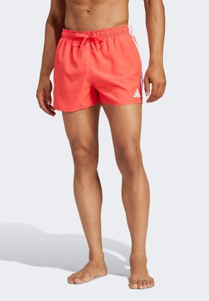 Shorts da nuoto color corallo con vita elasticizzata, coulisse e tre strisce bianche sui lati. Presenta un logo Adidas sul lato sinistro della gamba.