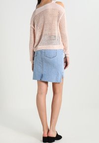 Jasnoróżowy sweter dzianinowy z otwartymi ramionami, w połączeniu z niebieską denimową spódnicą mini z postrzępionymi brzegami i bocznymi rozporkami. Czarne buty.