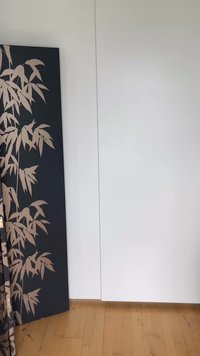 Πτυσσόμενος διαχωριστής χώρου με σχέδιο μπεζ φύλλων μπαμπού σε μαύρο φόντο, τοποθετημένος σε ξύλινο πάτωμα μπροστά σε λευκό τοίχο.
