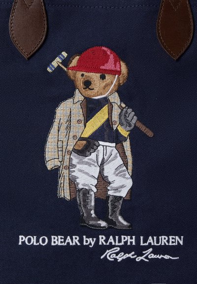 Brodert teddybjørn som har på seg rød hjelm, rutete kåpe, ridebukser og støvler, holder en polokølle, med teksten Polo Bear av Ralph Lauren.