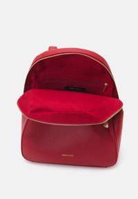 Sac à dos en cuir rouge avec une fermeture éclair, un extérieur lisse et un intérieur en tissu rouge contrastant doté d'une poche zippée et d'un logo embossé.