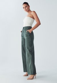 Zelené široké nohavice s vysokým pásom a záhybmi, v kombinácii s bielym rebrovaným topom bez ramienok. Celý vzhľad dopĺňajú sandále na priehľadnom podpätku.