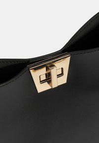 Zwarte leren handtas met een gladde textuur, voorzien van een gouden metalen sluiting en een minimalistisch ontwerp. Het interieur is onopgemaakt.