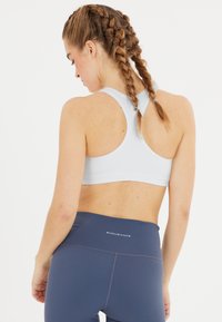 Ljust grå sport-bh med racerbackdesign, i kombination med marinblå högmidjade leggings som har "ENDURANCE"-logotypen på midjan.