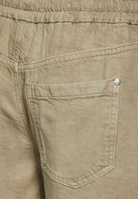 Beige cotton pants featuring an elastic waistband, back pocket, and tonal stitching. The texture is smooth with a slight sheen.