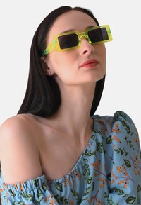 Grüne durchsichtige rechteckige Sonnenbrillen mit dunklen Gläsern, die ein mutiges geometrisches Design und klare Hardware-Details aufweisen.