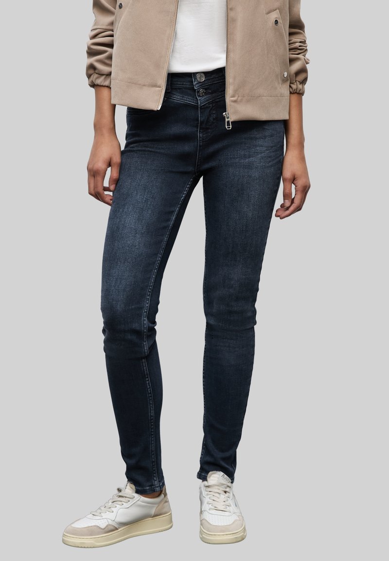 Ciemnoniebieskie rurki wykonane z denimu, charakteryzujące się gładką fakturą i dopasowanym krojem, zestawione z jasnymi trampkami.