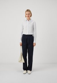 Biała, w paski koszula z długim rękawem, zestawiona z granatowymi spodniami o szerokich nogawkach i kremowymi butami wsuwanymi. Trzyma jasnobeżową torebkę.