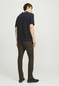 Polo a maniche corte blu navy con tessuto strutturato, abbinato a pantaloni marroni e scarpe nere, visto da dietro. Design del colletto semplice.