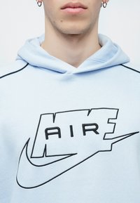 Lichtblauwe hoodie met een frontafbeelding waarop "AIR" in het zwart staat, samen met een zwarte Nike-swoosh. Gemaakt van zachte stof met een ontspannen ontwerp.