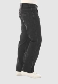 Jeans de mezclilla negra con un corte recto, que cuentan con una cintura resistente, trabillas para cinturón y dos bolsillos traseros; combinados con zapatillas blancas.