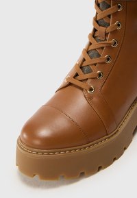 Botte en cuir marron avec un bout arrondi, un accent en tissu gris texturé et une semelle épaisse en forme de coin avec un motif de marche robuste.