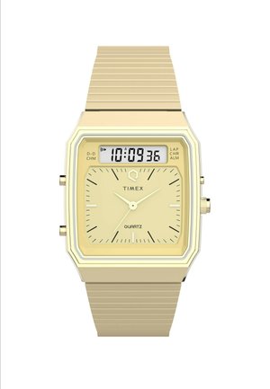 Kvarts Timex kell ruudukujulise kuldtooniga korpusega, digitaalse ekraaniga ja tekstuuriga kuldtooniga metallist rihmaga. Omab tunni ja minuti näitajaid.