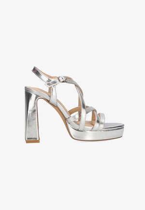 Sandal de tacón alto de metal plateado con plataforma, que presenta correas entrelazadas y una correa en el tobillo con hebilla. Textura suave y diseño de tacón cuadrado.