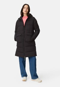 Black puffer coat with a hood, front zipper, and two large pockets. The coat is knee-length and features a quilted texture. Worn over a pink shirt.