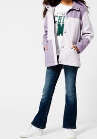 Světle fialová a bílá bunda s kapucí, se zacvakávacími knoflíky a kapsami, přehozená přes bílou grafickou mikinu a modré džíny. Bílé tenisky.