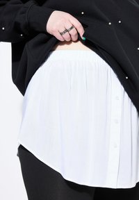 Sudadera negra con detalles de perlas, superpuesta a una camisa blanca de botones con cintura elástica y dobladillo curvado, combinada con leggings negros.