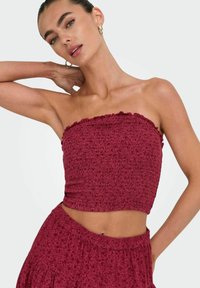 Bordeaux strapless crop top med struktureret stof, flæser i kanten og tætsiddende design, parret med en matchende nederdel med blomstermønster.