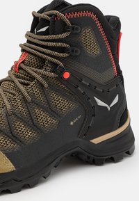 Turse sko med et svart og olivengrønt design, teksturert overflate, røde detaljer og et GORE-TEX-logo for vanntett ytelse.
