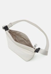 Beige schoudertas met een gladde canvas buitenkant, ritssluiting en verstelbare schouderriem. De binnenzijde heeft een logo-voering en een vak.