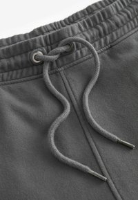 Graue Jogginghosen mit einem Kordelzugverschluss. Der Bund hat eine gerippte Textur, und die Kordel hat silberne Aglets. Weicher Stoff.