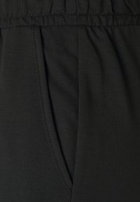 Schwarze Baumwoll-Sweatpants mit elastischem Taillenbund, seitlichen Taschen und dezenten Nahtdetails. Weiche Textur mit glatter Oberfläche.